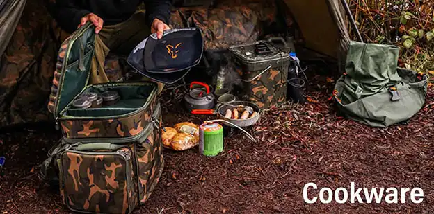 A man sits in front of a tent, holding a bag of food, surrounded by nature